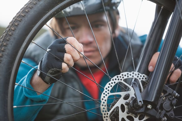 Male mountain biker examining front wheel of his bicycle in the forest